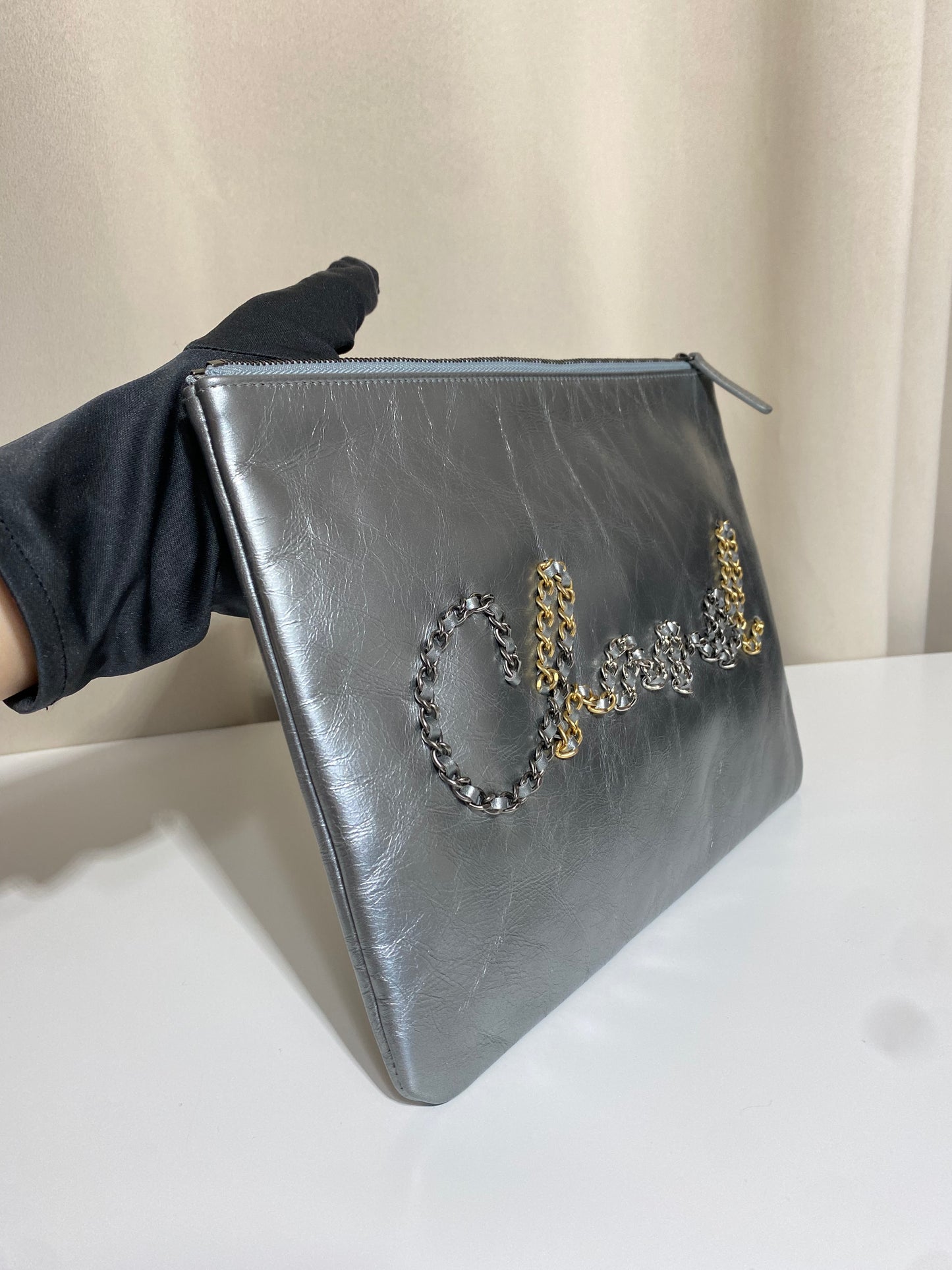 Pochette Chanel O Case Clutch en cuir de veau argent métallisé avec logo chaîne dorée et ruthénium – Très bon état d’occasion – Héritage du Luxe