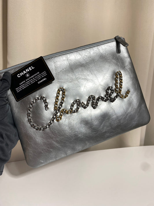 Pochette Chanel O Case Clutch en cuir de veau argent métallisé avec logo chaîne dorée et ruthénium – Très bon état d’occasion – Héritage du Luxe